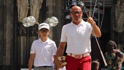 Auf dem Foto zu sehen sind Stephan Wasserkordt und sein kleiner Sohn Paul im Golfoutfit und mit einer Miniatur des "Häts för Kölle" vor der Kulisse des Kölner Doms. Wasserkordt hält zudem einen Golfschläger in der Hand.