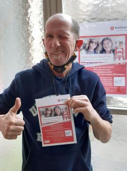 Ein regelmäßiger Gast des Kölner Wohlfühlmorgens hält das aktuelle Plakat in den Händen. Er ist froh über das neue Angebot „Warm durch den Winter“. Foto: Malteser Köln