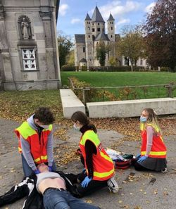Vor der Kulisse des Schlosses Knechtsteden versorgen zwei Schulsanitäterinnen und ein Schulsanitäter einen verletzt vor ihnen liegenden Motorradfahrer. 
